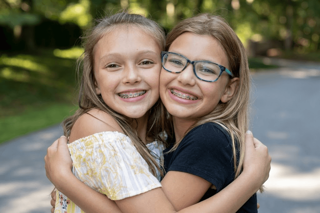 Two girls hugging outdoors, both wearing braces